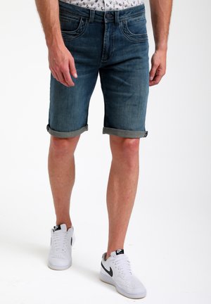 Shorts en denim bleu moyen, avec des poignets roulés, design à cinq poches, associés à des baskets blanches avec des accents noirs et des détails perforés.