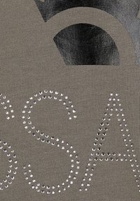 Olive green fabric featuring a textured pattern with shiny rhinestones forming the letters "S A" and a graphic design in black above.