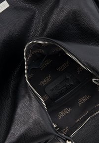 Zwarte leren handtas met een gestructureerd uiterlijk en een zilveren ritssluiting. Het interieur heeft een merkgevoerd stoffen voering in donkere tinten en een klein ritsvak.