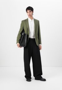 Blazer verde, camisa blanca, pantalones negros oversized y un bolso negro. El blazer tiene un acabado texturizado y solapas simples.