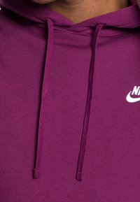 Lila huvtröja med en mjuk textur, snörning och en vit Nike-logotyp på bröstet.