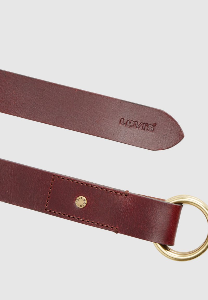 Cintura in pelle marrone con fibbia circolare dorata. Presenta logo in rilievo e dettagli cuciti. Texture liscia e design con estremità rastremata.