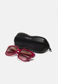 Czerwone okulary przeciwsłoneczne z kwadratowymi oprawkami, gradientowymi soczewkami oraz brokatowymi akcentami. W zestawie z czarnym etui na zamek błyskawiczny z logo "vogue".