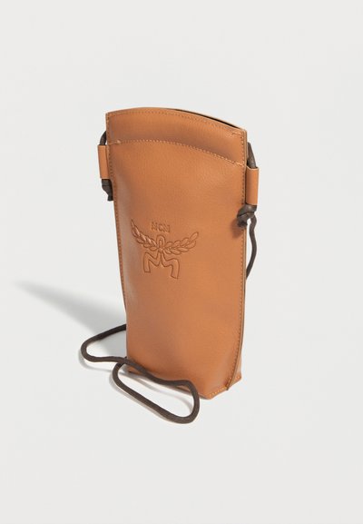 Tall tan leather crossbody pouch with embossed MCM logo and dark adjustable strap on a white background.
