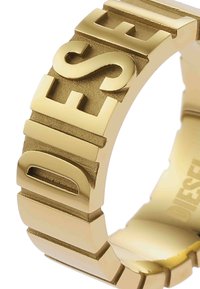 Bague en m�étal doré avec des lettres 3D audacieuses. Surface texturée avec des accents lisses, mettant en valeur un design géométrique moderne.