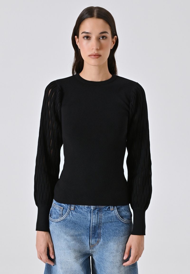 Schwarzer Strickpullover mit langen, strukturierten Puffärmeln. Figurschnitt, runder Ausschnitt, kombiniert mit hellblauen, verwaschenen Jeans.