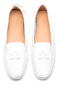 Bijele kožne cipele na slip-on s teksturiranom površinom, ušivenim detaljima i istaknutim bijelim logotipom sprijeda. Glatka unutarnja podstava.