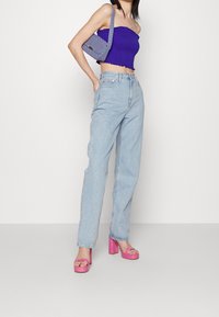 Haut court smocké violet, jean taille haute bleu clair et sandales compensées roses. Petit sac gris avec bandoulière.