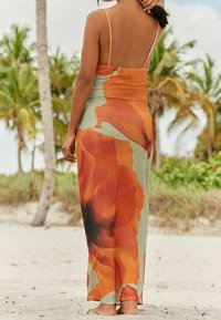 Robe longue à motif floral en orange et vert, avec des fines bretelles et un corsage ajusté se transformant en jupe fluide.
