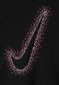 Logo de Nike en forma de swoosh formado por pequeños puntos rojos, rosas y blancos dispersos sobre un fondo negro.