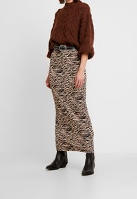 Brown knitted sweater with a high neckline, paired with a knee-length zebra print skirt in beige and black, complemented by black ankle boots.