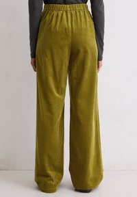 Olijfgroene wijde corduroy broek met een gestructureerd oppervlak, elastische tailleband en een strakke, onopgesmukte uitstraling.