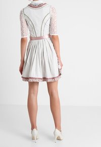 Robe blanche avec des manches courtes en dentelle, ceinture rose à la taille, motif à pois et bord floral à l'ourlet, associée à des escarpins blancs.