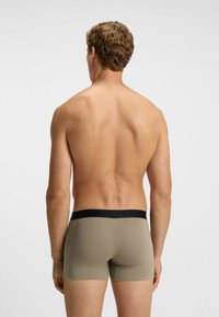 Beige Boxershorts mit schwarzem elastischem Bund, figurbetontem Schnitt und glattem Stoff. Das Modell ist von hinten zu sehen.