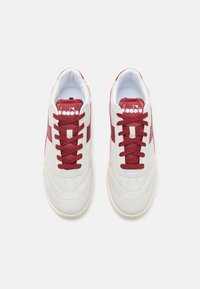 Hvite semskede sneakers med burgunder detaljer og lisser. Teksturt overdel og gummisåle, med en logo på tungen og siden.