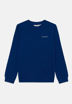 Granatowy sweter z bawełny, z okrągłym dekoltem i prążkowanymi mankietami. Ma małe, białe logo Calvin Klein na klatce piersiowej.