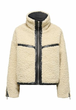 Veste en peau retournée de couleur crème avec une fermeture éclair noire à l'avant, des rayures horizontales noires contrastantes, un col montant et des poignets zippés.