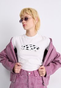 White t-shirt featuring a black and white rabbit graphic, layered under a light pink denim jacket. Textured fabric with a relaxed fit.