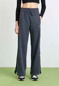 Grå sweatpants med vita sidosträck, dragsko i midjan och vid ben design, tillverkade av mjukt tyg. Nike-logotypen på framsidan.