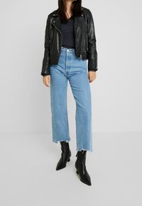 Svart läderbikerjacka, marinblå topp, högmidjade ljusblå jeans med slitna kanter, och svarta spetsiga ankelstövlar.