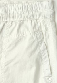 Gros plan d'une ceinture élastique blanche avec une poche latérale cousue comportant un petit rivet métallique sur un tissu léger.