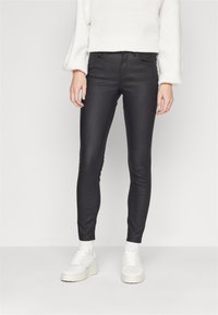 Jeans negros entallados con una textura suave y detalles de costura sutiles, combinados con un suéter blanco texturizado y zapatillas blancas.