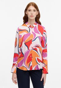 Langærmet skjorte med knaplukning i let materiale, prydet med et farverigt blomsterdesign med svirvler af pink, orange og rød på en hvid baggrund.
