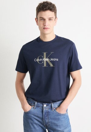 Camiseta de algodón azul marino con cuello redondo y mangas cortas, que presenta un logo impreso en dorado "Calvin Klein Jeans" en el frente.