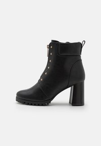 Černá kožená kotníková bota s kulatou špičkou, robustním podpatkem, bočním zipem a zlatými hřebíčky podél vnější strany pro přidaný detail.