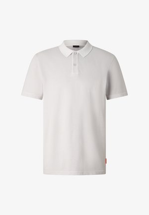 Polo blanc à manches courtes avec deux boutons et un col, présentant une broderie discrète du logo sur le côté gauche de la poitrine et une petite étiquette rouge sur le côté.