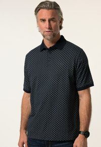 Tummansininen polo-paita lyhyillä hihoilla, jossa on geometrinen kuvio ja kontrastivärinen kaulus. Pehmeä pinta, jossa nappilista yksityiskohtana.