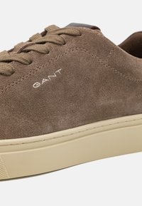 Braune Wildleder-Sneaker mit beiger Gummisohle, ausgestattet mit tonal passenden Schnürsenkeln und dem in Weiß auf der Seite gestickten "GANT"-Logo, schlichtes Design.