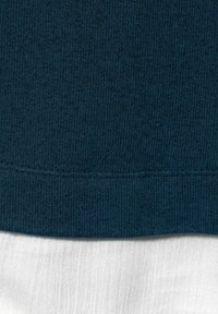 Mörkblå ribbad stickad tyg lager på slät vit tyg, som visar tydlig textur och en horisontell sömlinje över det blåa tyget.