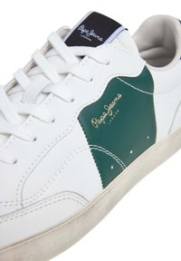 White sneaker with green leather side panel, white laces, and textured rubber sole. Features “Pepe Jeans” logo in gold on side.