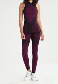 Conjunto deportivo en púrpura y negro que presenta una camiseta sin mangas ajustada con un escote alto y leggings a juego con patrones geométricos, combinados con zapatillas blancas.