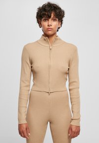 Beige ribbade zip-up topp med hög krage, långa ärmar och en figurnära passform, med en guldfärgad dragkedja framtill.
