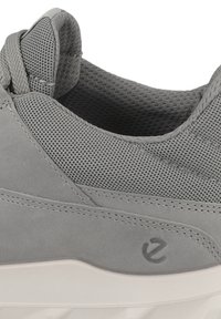 Baskets grises en suède et maille, avec un dessus texturé, un col rembourré et un logo discret sur le côté, le tout reposant sur une semelle en caoutchouc blanche.