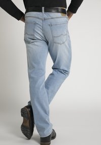 Helle blaue Jeans im Straight-Leg-Schnitt, mit zwei hinteren Taschen und geschwungener Naht, getragen mit einem schwarzen Gürtel und Schuhen.