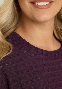 Lila strukturerad tröja med ribbad halsringning. Tyget har ett vågigt mönster, och skärningen är löst sittande runt halsen och axlarna.