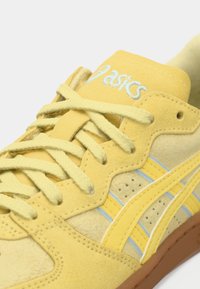 Κίτρινα σουέτ αθλητικά παπούτσια με ταιριαστά κορδόνια, διάτρητη λεπτομέρεια και ανοιχτού μπλε λεπτομέρειες. Διαθέτει καφέ λάστιχο σόλας και λογότυπο στη γλώσσα.