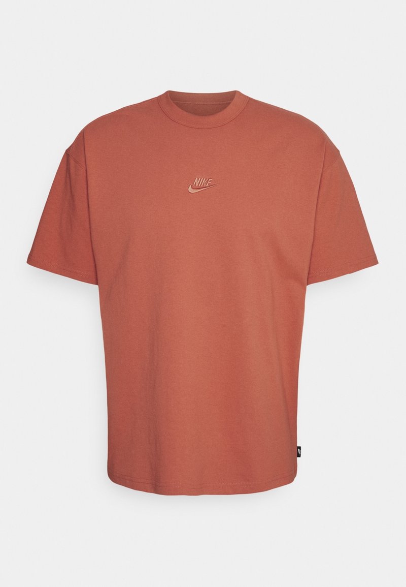 T-shirt Nike de couleur rouille en coton. Il présente un col rond, des manches courtes et un logo brodé sur la poitrine dans une teinte plus claire.