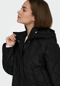 Czarna pikowana kurtka z zamkiem błyskawicznym i zatrzaskami, kapturem oraz bocznymi kieszeniami. Charakteryzuje się gładką fakturą i dopasowanym krojem.