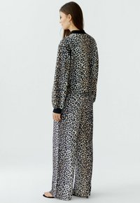 Loungewear-Set im Leopardenmuster mit langärmeligem Oberteil und schwarzem Bündchen sowie weit geschnittenen Hosen, aus weichem Stoff mit glatter Textur.