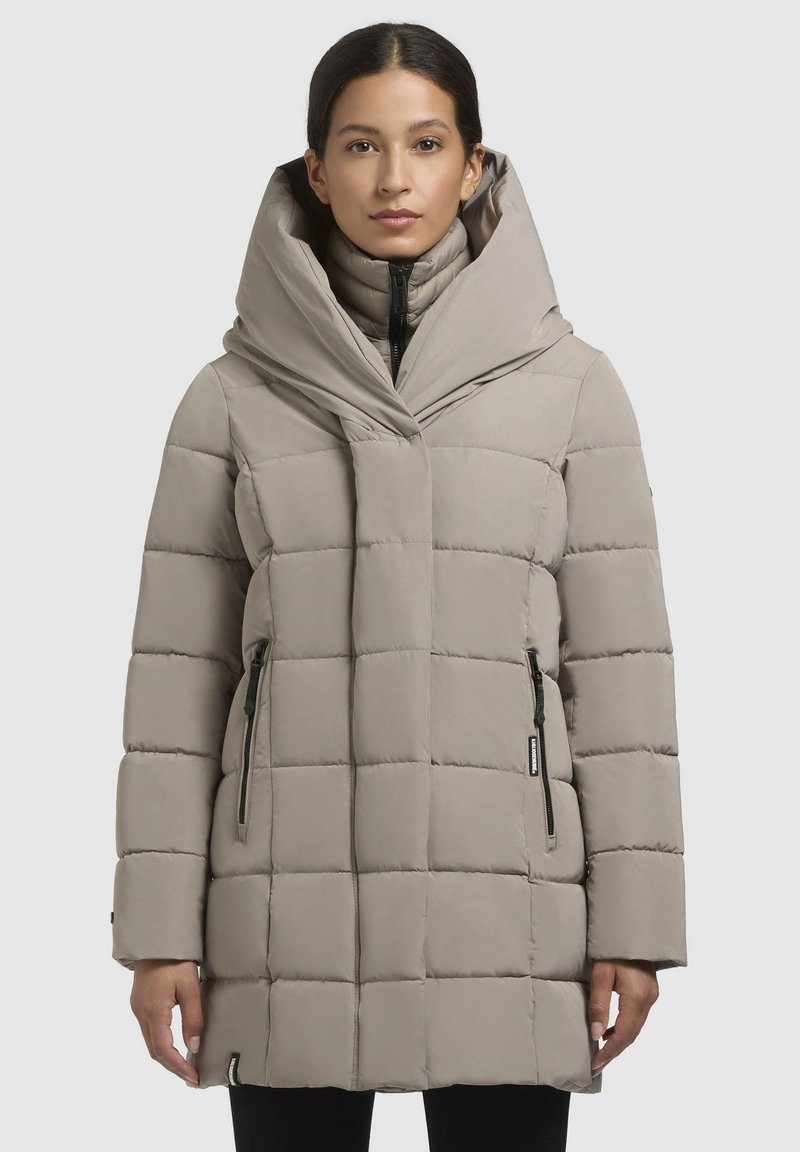 Manteau en duvet gris clair, doté d'un col oversize unique, d'un motif matelassé, de deux poches latérales zippées et d'une fermeture éclair à l'avant.