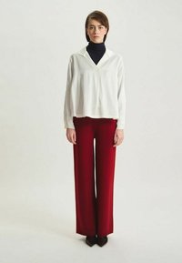 Blouse blanche avec un col, associée à un pantalon rouge à jambes larges. La blouse présente une coupe décontractée et une texture douce.
