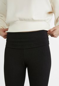 Mustat legginsit, joissa on leveä, pehmeä vyötärönauha. Kangas näyttää sileältä ja joustavalta, suunniteltu mukavaksi ja vartalonmyötäiseksi käytettäväksi.