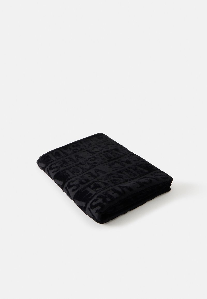 Serviette noire pliée avec motif de texte en relief sur un fond blanc uni.