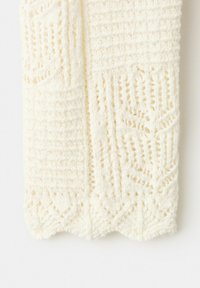 Tissu tricoté de couleur crème avec un motif géométrique en dentelle et des bords festonnés, montrant une texture détaillée et un design ajouré.