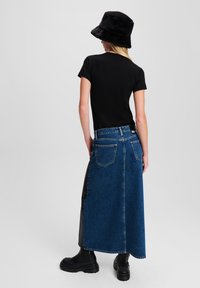 Denim maxi szoknya fekete műbőr oldalsó panellel, öt zsebbel, magas derékkal, fekete pólóval és fekete vödörkalappal párosítva.