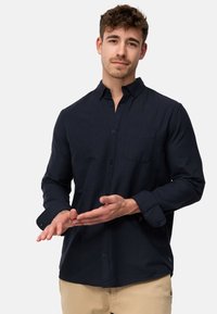 Camisa de botones color navy hecha de algodón, con un bolsillo en el pecho, mangas largas con puños abotonados y un dobladillo recto.